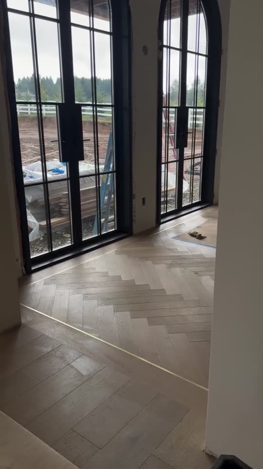 Finished herringbone oak floor by Grand Com in a room with tall arched steel windows